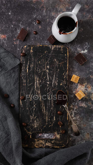 Black scratched cutting board next to coffee beans and dark chocolate — Fotografia de Stock