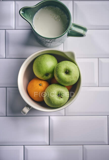 Pommes et oranges dans un bol en céramique avec cruche à lait — Photo de stock
