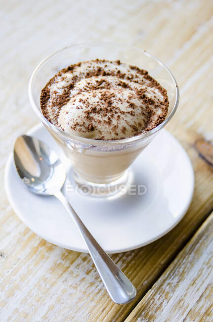 Eiskaffeesahne mit geriebener Schokolade im Glas auf Untertasse mit Löffel — Stockfoto