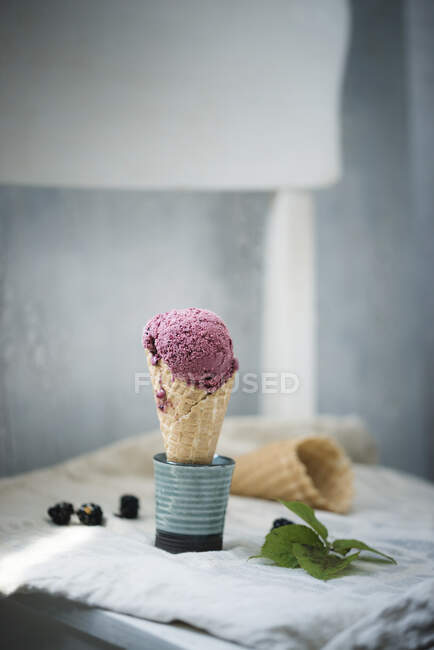 Веганское ежевичное мороженое в вафельном рожке, конусе и ягодах на заднем плане — стоковое фото