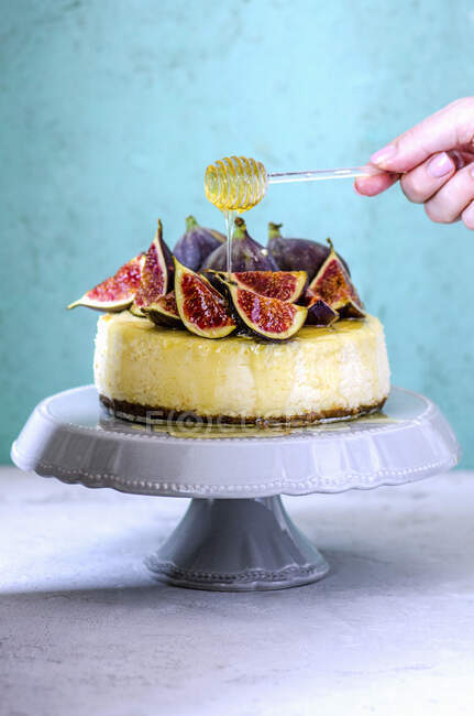 Cheesecake with figs and honey and hand holding stick with dripping honey — Stock Photo