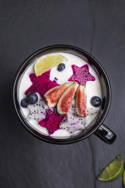 Fruta fresca com iogurte em tigela na superfície escura — Fotografia de Stock