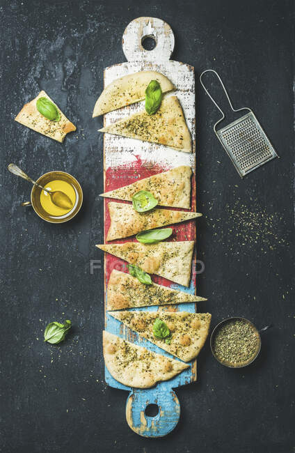 Homemade Italian focaccia flatbread cut into pieces with herbs, fresh basil leaves, olive oil and glass of rose wine — Stock Photo