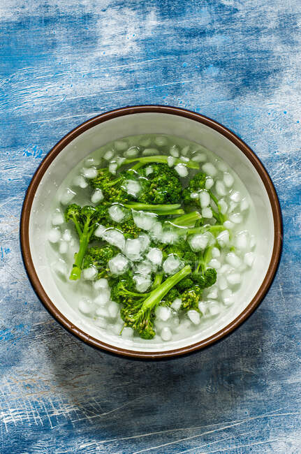 Blanched broccoli in ice water in bowl on blue old background — Stock Photo