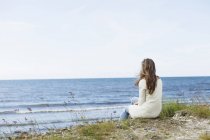 Женщина, сидящая на пляже против неба — стоковое фото