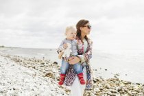 Madre sosteniendo hijo en playa - foto de stock
