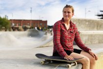 Donna con skateboard seduta sulla rampa allo skate park — Foto stock