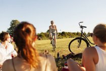 Man cycling while friends relaxing on field — Stock Photo