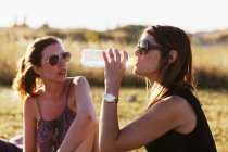 Woman sitting by friend and drinking water — Stock Photo