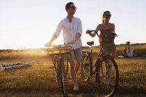 Friends walking with bicycles on field — Stock Photo