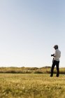 Hombre sosteniendo la cámara y de pie en el campo - foto de stock