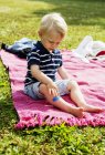 Хлопчик з пов'язкою на нозі сидить на ковдрі для пікніка — стокове фото
