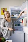 Жінка дивиться геть, стоячи біля відкритого холодильника — стокове фото