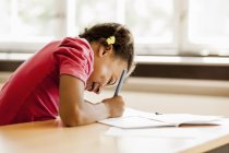 Schoolgirl writing in book at desk — Stock Photo