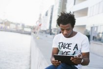 Student using digital tablet by river — Stock Photo