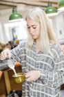 Joven barista hembra vertiendo leche - foto de stock