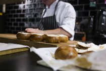 Chef tranchant des petits pains au comptoir de la cuisine — Photo de stock