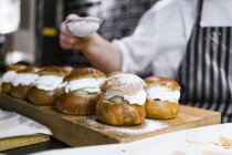 Chef époussetant du sucre glace sur des petits pains à la crème — Photo de stock