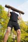 Young man lifting log at park — Stock Photo