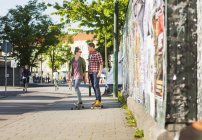 Happy couple skateboarding on sidewalk — Stock Photo