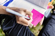 Estudiante escribiendo en nota adhesiva en libro - foto de stock