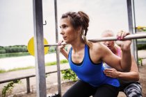 Woman helping friend in lifting barbell — Stock Photo