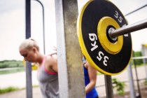 Woman helping friend in lifting barbell — Stock Photo