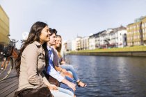 Friends sitting on floorboard by canal — Stock Photo