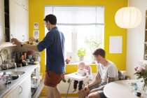 Gay couple with baby girl in kitchen — Stock Photo