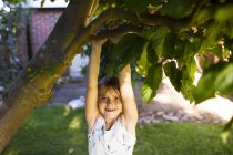 Happy girl hanging from branch — Stock Photo