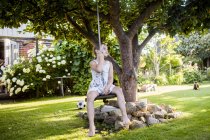 Fille assise sur swing dans le jardin — Photo de stock