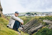 Mann hält Kamera während er auf Hügel sitzt — Stockfoto