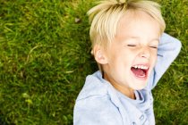 Menino rindo enquanto deitado na grama — Fotografia de Stock