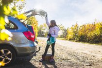 Girl looking into open car trunk — Stock Photo