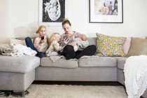 Girls sitting by mother on sofa — Stock Photo
