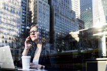 Donna d'affari utilizzando il telefono visto attraverso la finestra — Foto stock