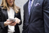Бизнесмен и деловая женщина, стоящие со смартфоном — стоковое фото