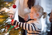 Mãe ajudando filha na decoração da árvore de Natal — Fotografia de Stock