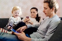 Mädchen sitzt neben Eltern und nutzt Technologien — Stockfoto