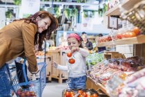 Chica sosteniendo tomates mientras está de pie por madre - foto de stock