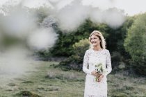 Mariée tenant bouquet dans la forêt — Photo de stock