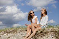 Веселые друзья сидят на песке — стоковое фото