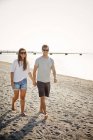 Couple tenant la main tout en marchant sur le rivage — Photo de stock