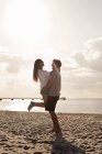 Homem carregando namorada na praia — Fotografia de Stock