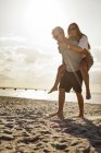 Paar genießt Huckepack-Fahrt am Strand — Stockfoto
