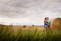Пара, стоящая у тюка сена на поле — стоковое фото