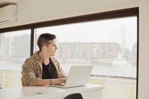 Man with laptop looking through window — Stock Photo