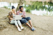 Couple using laptop at lake shore — Stock Photo