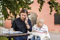 Uomo nutrire la bambina e parlare su smartphone — Foto stock