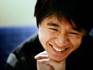 Portrait of smiling asian man with hands on chin and eyes closed — Stock Photo
